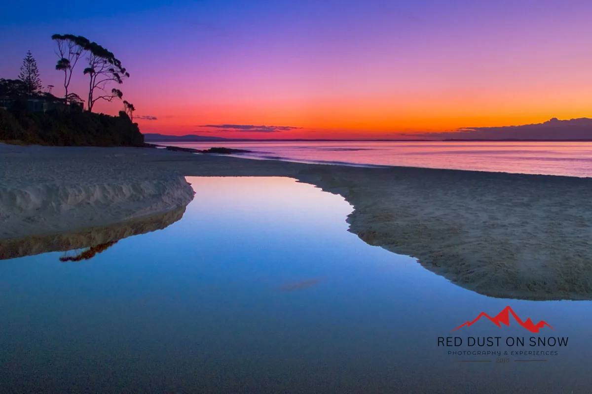 Winter sunrise at Hyams Beach, Jervis Bay, with pink and orange sky reflected in a tidal pool on the sand